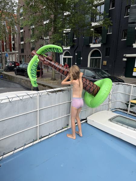 A child in pink underwear plays with a large inflatable palm tree on the blue deck of a houseboat in Oudeschans, Uilenburg, Amsterdam